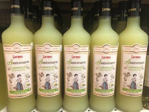 Five bottles of Lucano Limoncello lined up on a shelf, featuring a vintage label with a woman in traditional attire.