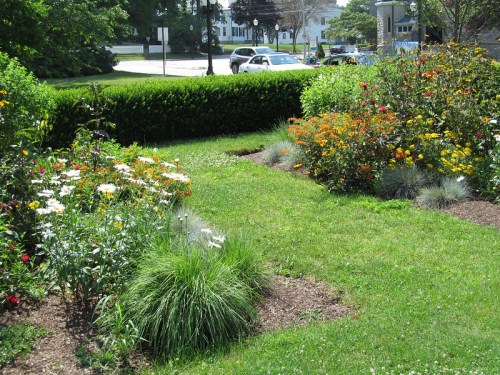A vibrant garden with colorful flowers and lush green grass, bordered by a neatly trimmed hedge.