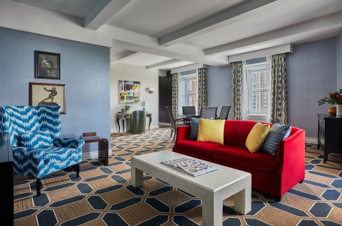 A stylish living room featuring a red sofa, blue patterned chair, and modern decor with a geometric rug.
