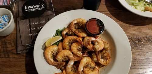 A plate of seasoned shrimp with a slice of lemon and a small cup of dipping sauce, set on a wooden table.