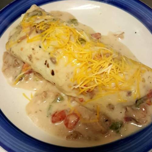 A plate featuring a burrito covered in creamy sauce and topped with shredded cheese, garnished with diced vegetables.