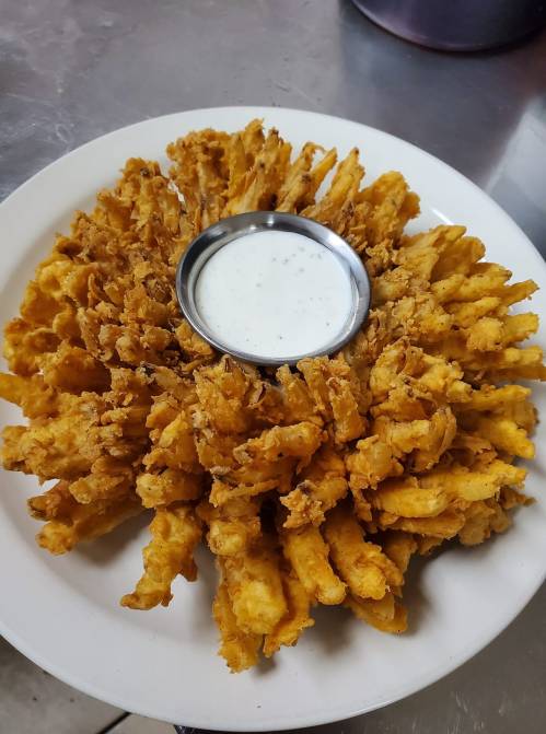 A large, golden-brown onion blossom served on a plate with a small bowl of dipping sauce in the center.