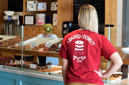 A person in a red shirt stands in front of a bakery display, with a staff member in the background.
