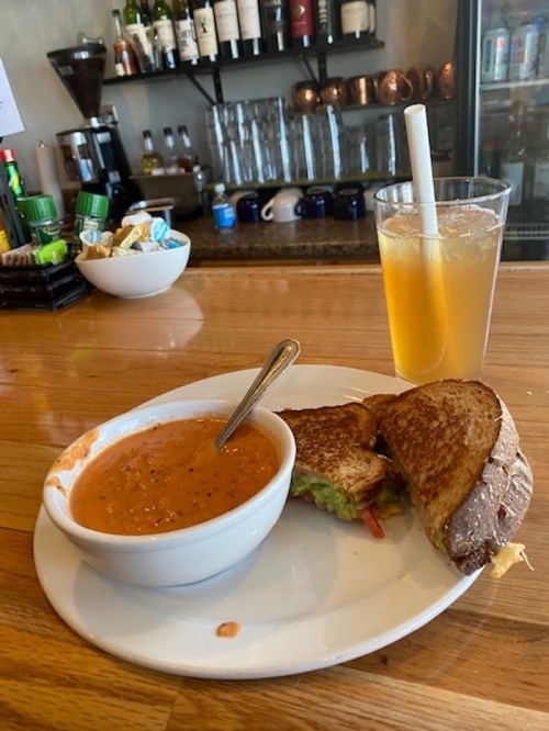 A bowl of tomato soup, a sandwich with lettuce and tomato, and a glass of iced tea on a wooden bar counter.