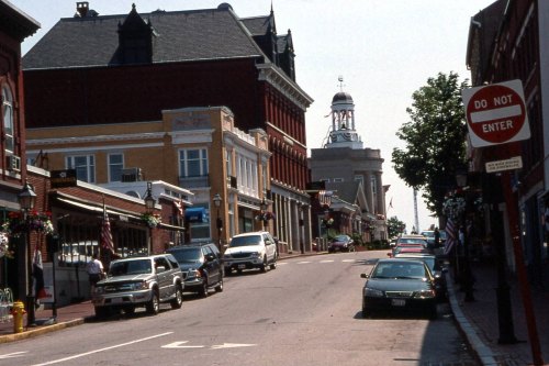 A quaint street lined with shops and parked cars, featuring a lighthouse in the background and a "Do Not Enter" sign.