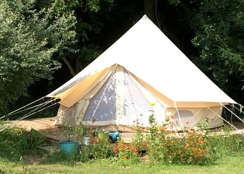 A white tent set on a wooden platform, surrounded by greenery and colorful flowers.
