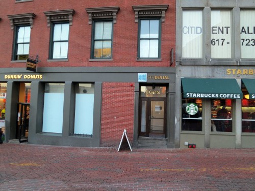 A brick building with Dunkin' Donuts and Starbucks Coffee storefronts, and a dental office entrance in between.