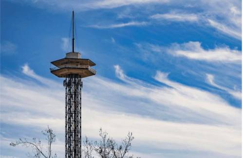 A tall observation tower with a flat roof against a blue sky with wispy clouds.