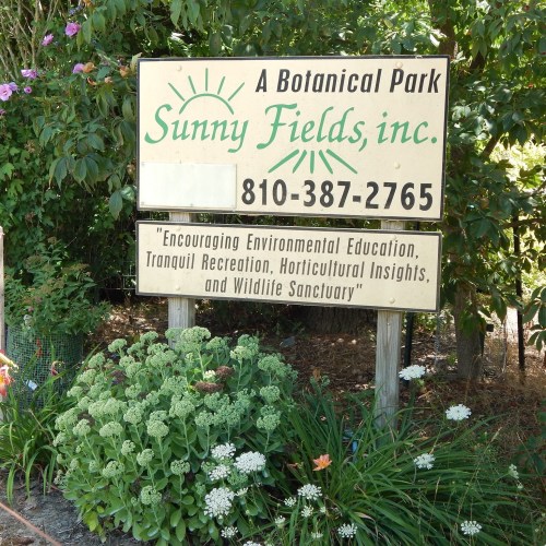 Sign for Sunny Fields Botanical Park, featuring contact info and a message about environmental education and wildlife sanctuary.