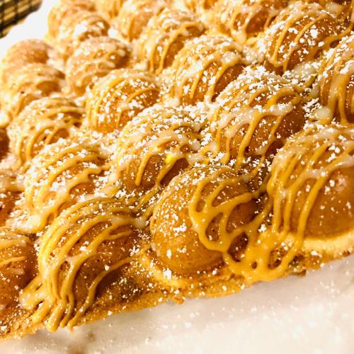 A close-up of a golden, bubble-shaped waffle drizzled with caramel and dusted with powdered sugar.