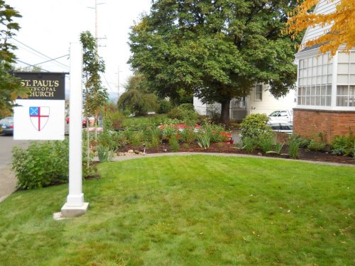A well-maintained church garden with green grass, flowers, and a sign for St. Paul's Episcopal Church.