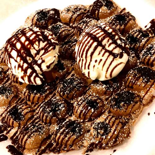 A plate of chocolate waffles topped with two scoops of ice cream and drizzled with chocolate sauce.