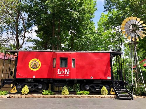 A red train caboose with "L&N" signage, surrounded by greenery and a windmill in the background.