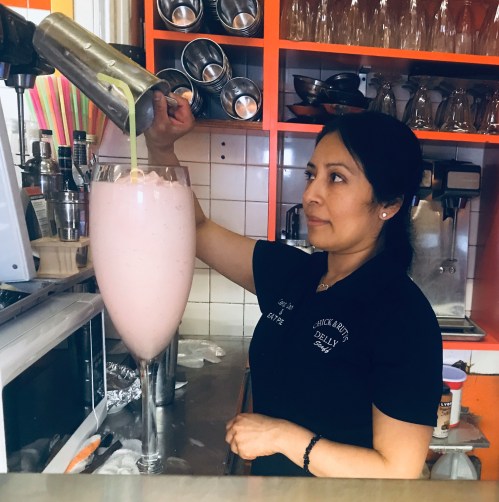 A woman prepares a large pink drink at a counter, pouring it into an oversized glass.