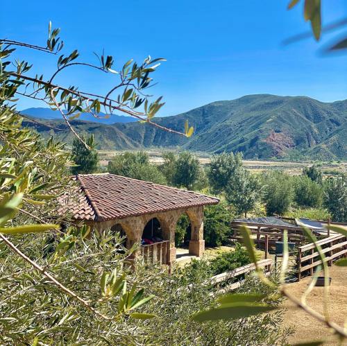 A rustic building with a tiled roof surrounded by trees and mountains under a clear blue sky.