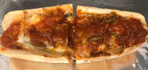 A split sandwich filled with melted cheese, marinara sauce, and sautéed vegetables on a toasted hoagie roll.