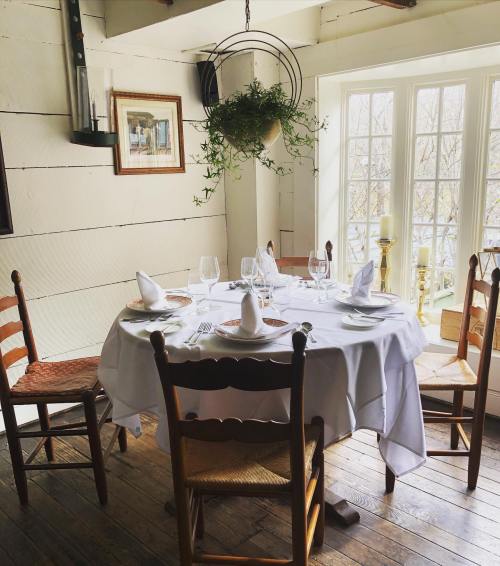 A cozy dining table set for four, adorned with white linens and glassware, near a window with natural light.