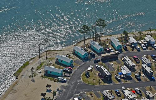Aerial view of a waterfront campsite with colorful cabins and RVs along a shimmering body of water.