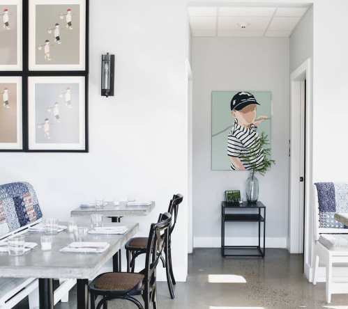 A modern dining space with artwork on the walls, featuring a table setting and a glimpse of a hallway.