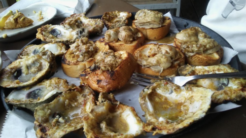 A platter of baked oysters and stuffed bread, garnished and served on a paper-lined tray.