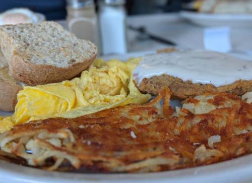 A plate of breakfast featuring scrambled eggs, hash browns, a biscuit with gravy, and slices of bread.