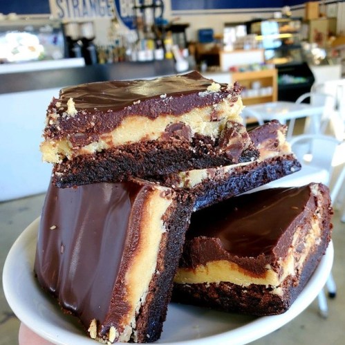 A plate of rich chocolate and cookie dough bars stacked together, set in a cozy café environment.