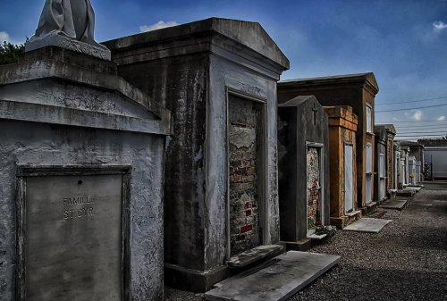 A row of weathered mausoleums in a cemetery under a blue sky, with some showing signs of age and wear.