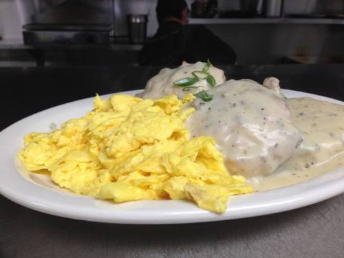 A plate of scrambled eggs and biscuits topped with creamy sausage gravy, garnished with green onions.