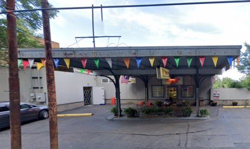 A small building with a covered entrance, decorated with colorful flags and surrounded by greenery.