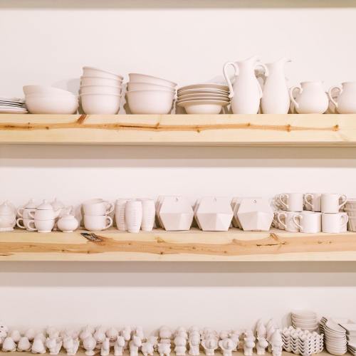 A display of white ceramic dishes and mugs arranged on wooden shelves.