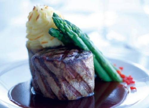 A gourmet dish featuring grilled steak, mashed potatoes, asparagus, and a rich sauce on a white plate.