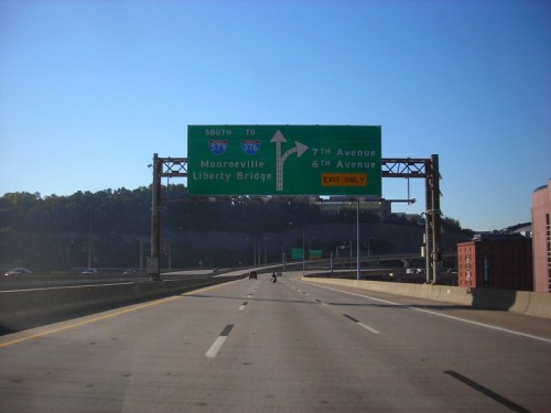 Highway sign indicating exit for Monroeville and Liberty Bridge, with directions for 7th and 6th Avenues. Clear blue sky.