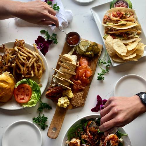 A spread of delicious food including tacos, fries, a burger, and a platter with various meats and pickles on a table.