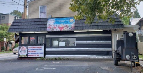 A small eatery with a black and white striped exterior, featuring an "Open" sign and a banner for ice cream.