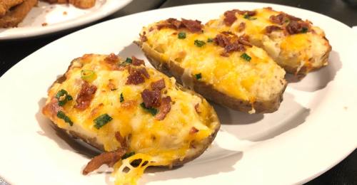 Three loaded baked potatoes topped with cheese, bacon, and green onions on a white plate.