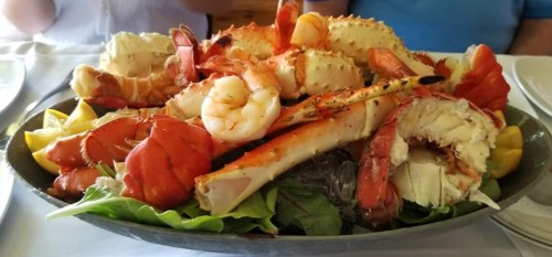 A large seafood platter featuring shrimp, lobster, crab, and lemon slices on a bed of greens.