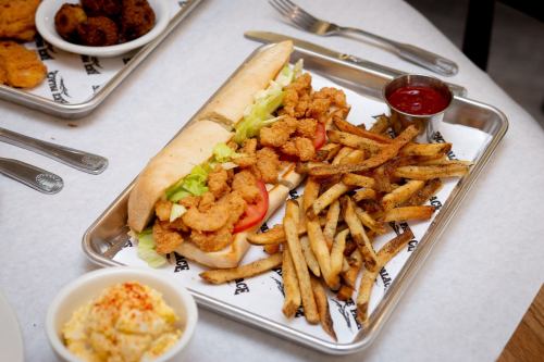 A sandwich filled with fried shrimp, lettuce, and tomato, served with fries and a side of ketchup on a tray.
