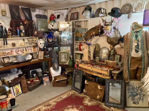 A cluttered room filled with eclectic decor, including masks, sculptures, and various vintage items on shelves and walls.