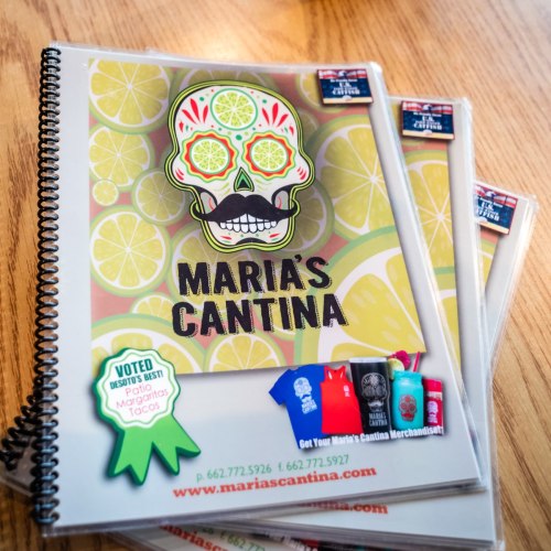 Menu covers for Maria's Cantina featuring colorful designs with limes and a skull motif on a wooden table.