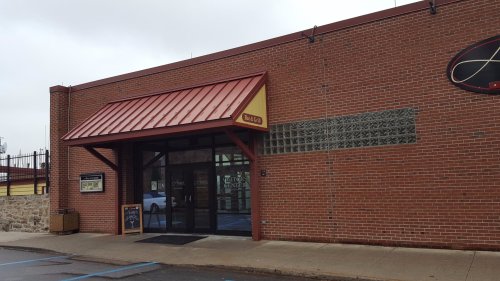 Exterior of a brick building with a red metal roof, featuring large glass doors and a sign.