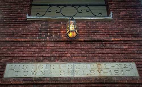 Historic brick wall with a lantern and a stone plaque reading "District School No. 1 Town of Shelby - 1917."