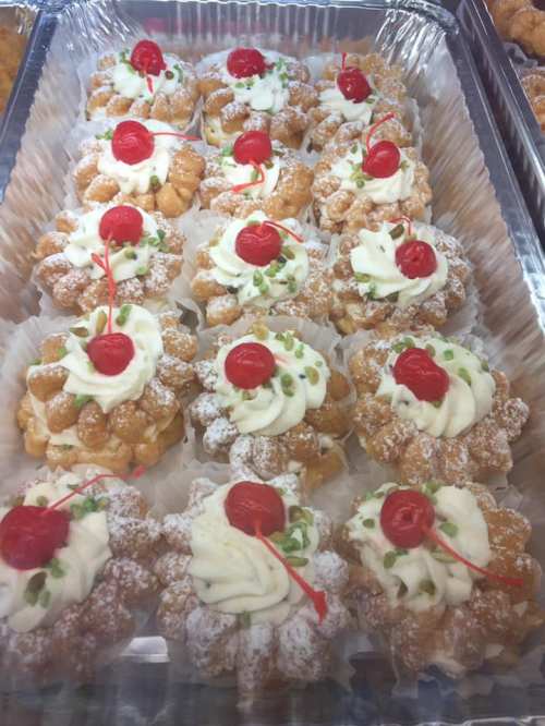 A tray of decorative pastries topped with whipped cream, cherries, and green sprinkles, arranged neatly.