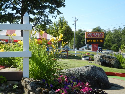 Colorful flowers and rocks in the foreground with a sign for Funspot, stating "Open All Year," in the background.