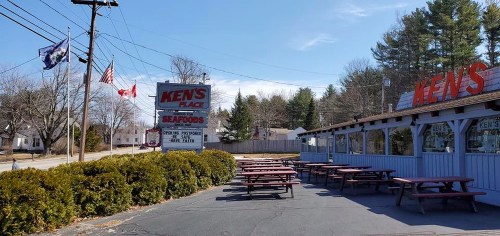 Exterior view of Ken's Place, a seafood restaurant, featuring picnic tables and flags on a sunny day.