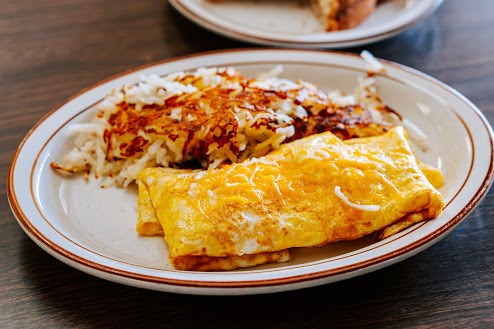 A plate with a cheese omelet and crispy hash browns, served on a wooden table.