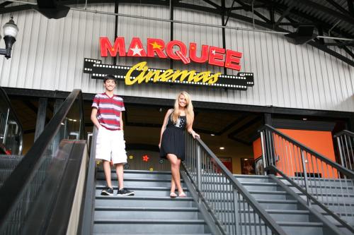 Two young people stand on stairs in front of a Marquee Cinemas sign, smiling and posing for the photo.