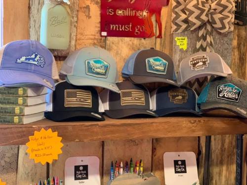 A display of various hats on a wooden shelf, featuring designs like flags and state-themed logos.