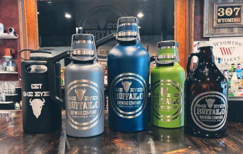 Five colorful growlers with "One Eyed Buffalo Brewing Company" branding, displayed on a wooden bar.