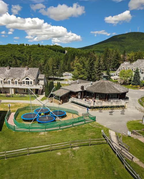 Aerial view of a resort area featuring trampolines, a restaurant, and lush green surroundings with a mountain in the background.
