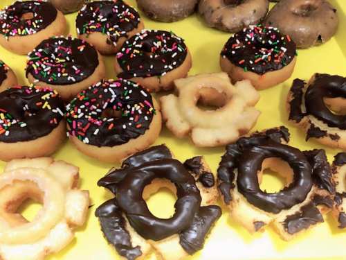 A variety of donuts, including chocolate frosted with sprinkles and unique shaped pastries, on a yellow background.